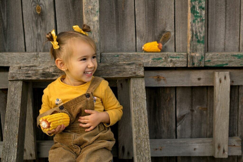 The girl is sitting on an old wooden staircase with corn in her hands